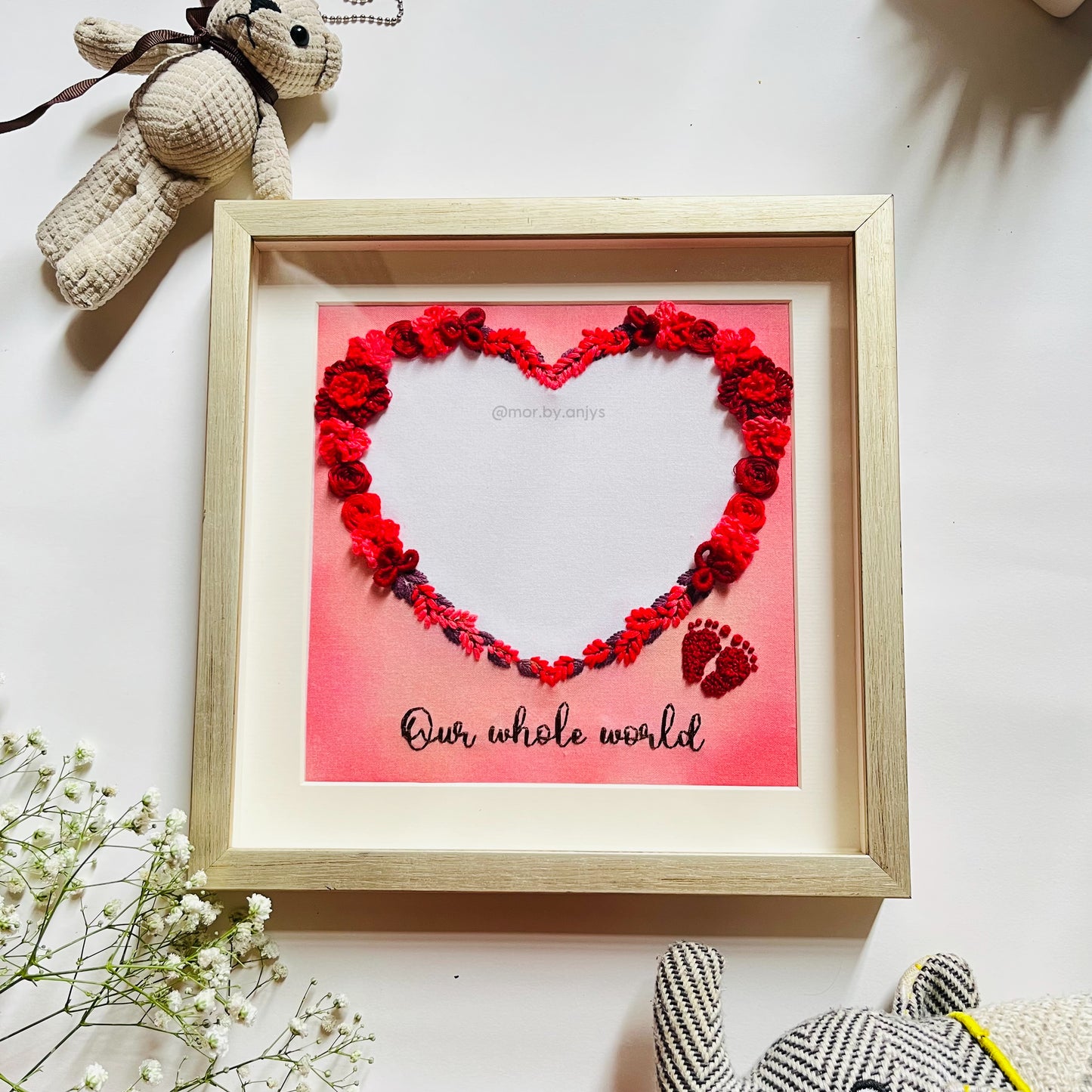 Framed artwork with red floral heart and text 'Our whole world' on a white background.