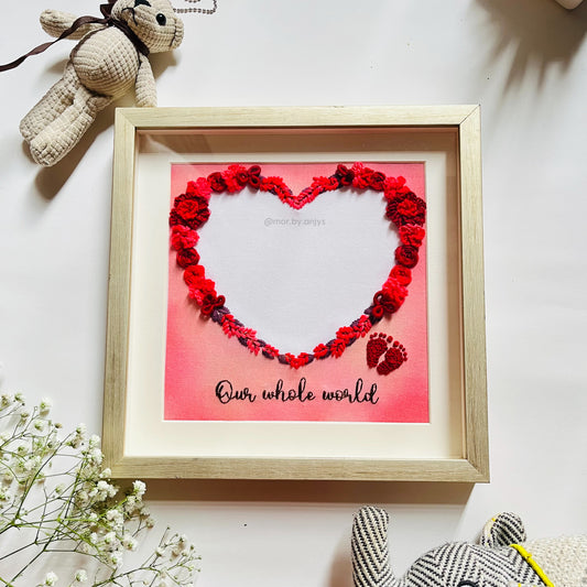 Framed artwork with red floral heart and text 'Our whole world' on a white background.